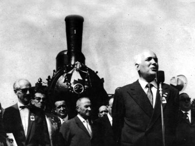 17 settembre 1961. All’inaugurazione del monumento parla Gino Bechi, presidente della Federazione Italiana Modellismo Ferroviario, nonché famoso baritono e attore dell’epoca. Alle spalle di Bechi, proprio sotto la ciminiera della locomotiva si può vedere lo storico macchinista della n.1 Giuliano Negri.